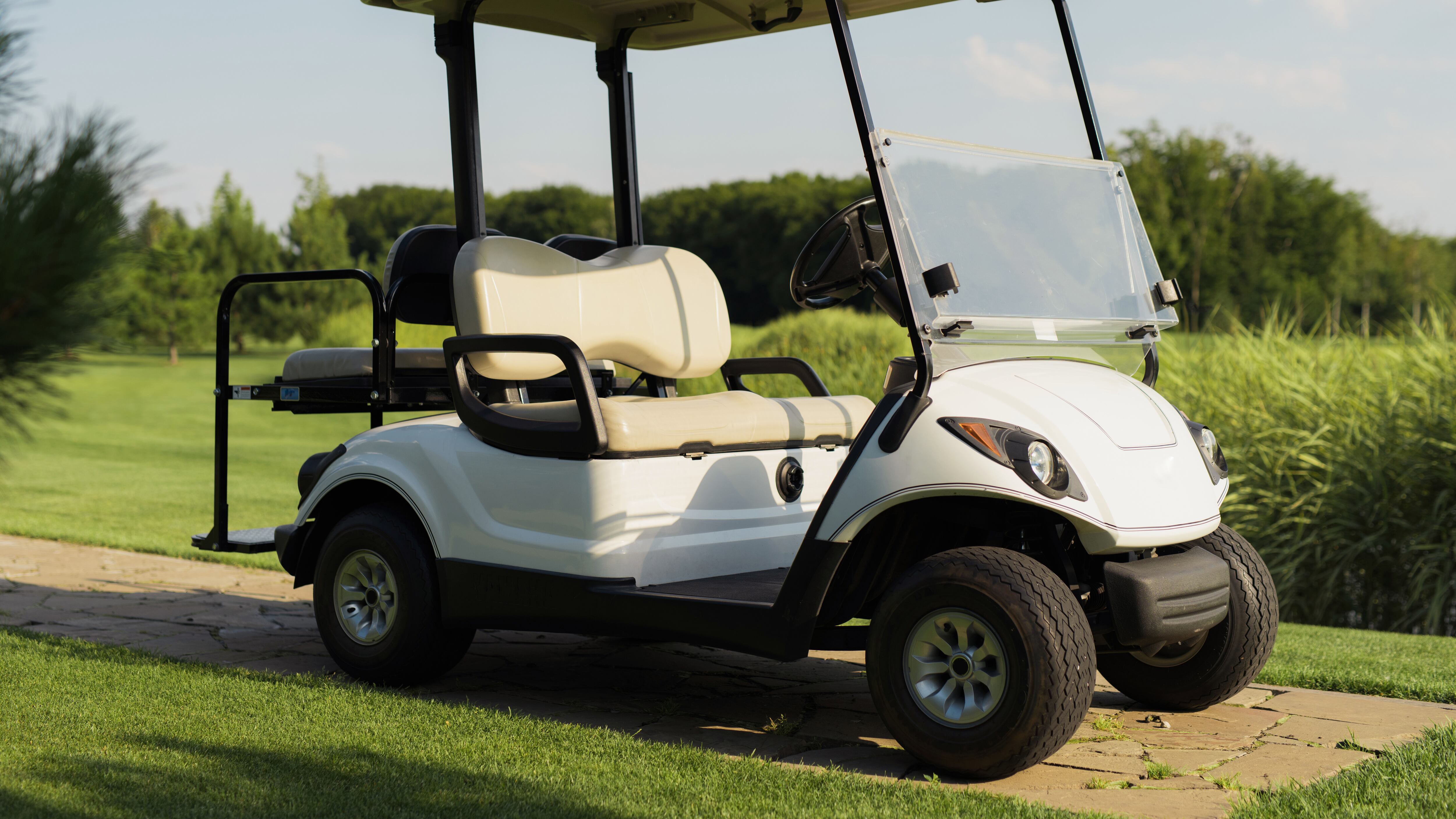 A white golf car stands on a stone path against the backdrop of a golf course