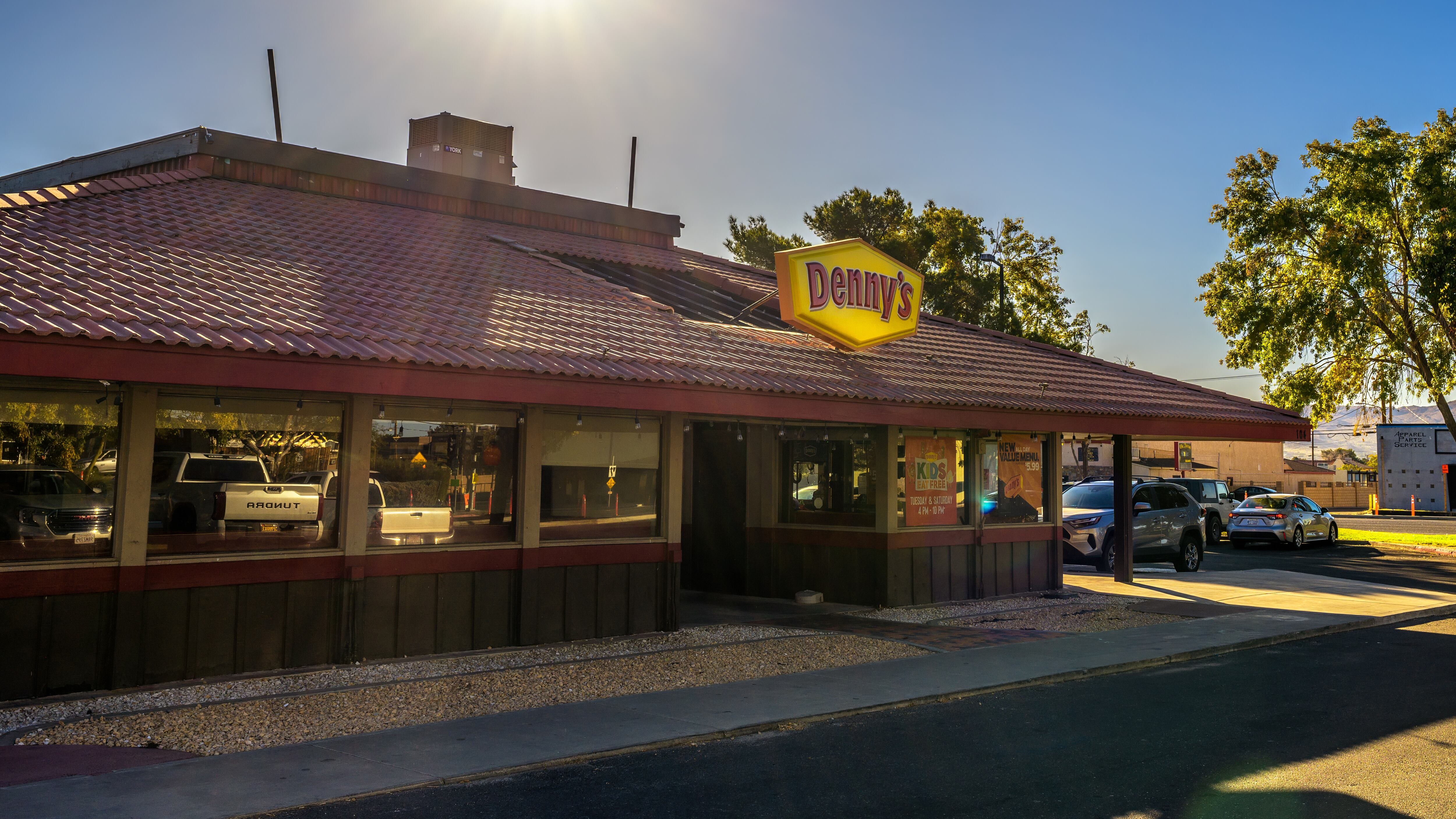 Sunrise over a vintage Denny's restaurant in Ridgecrest, California, with a neon sign and cars parked in the lot.